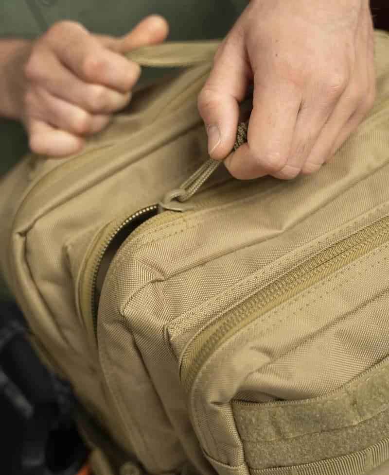 Bolsillo con cremallera de mochila táctica beige con correas de sujeción.