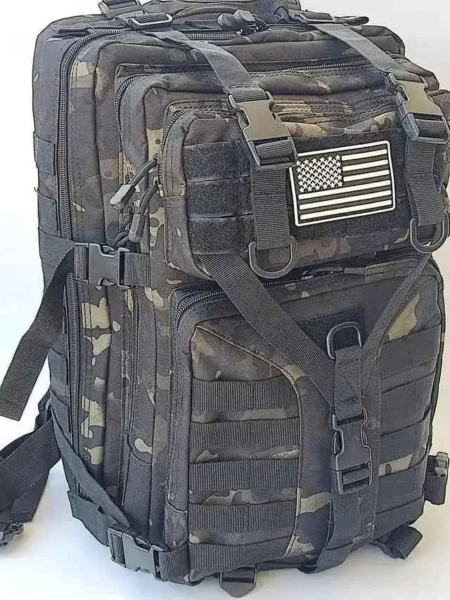 Mochila táctica camuflada con parche de bandera y bolsillos frontales con cremalleras.