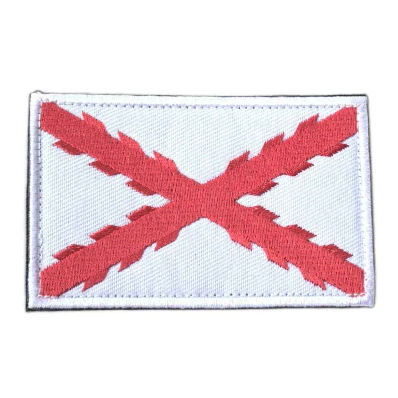 Parche rectangular de tela con bandera roja en aspa sobre fondo claro y borde blanco