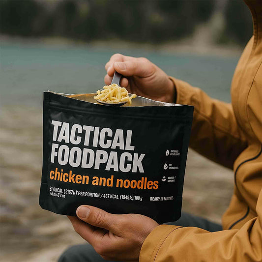 Bolsa negra con pollo y noodles, con una cucharada de fideos sobre el borde